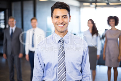 Businessman smiling at camera while her colleagues standing in b