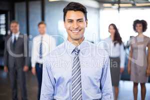 Businessman smiling at camera while her colleagues standing in b