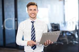 Portrait of businessman standing with a laptop in office