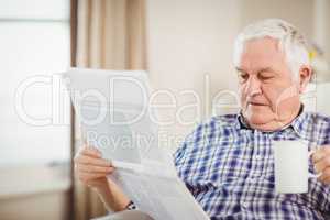 Senior man reading newspaper in living room