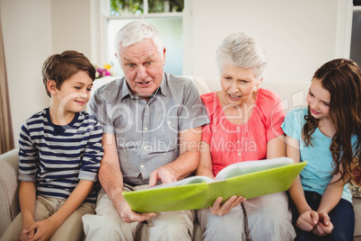 Senior couple reading a book with their grand children