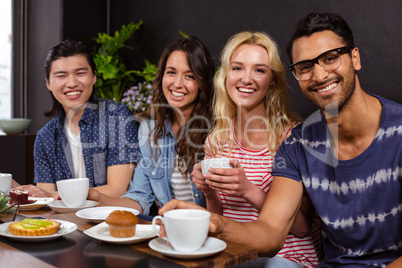 Smiling friends enjoying coffee together and using technologies