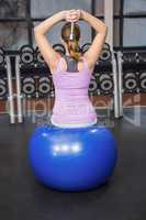 Determined woman lifting dumbbell on fitness ball