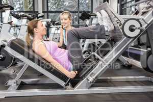 Trainer motivating pregnant woman while using leg press