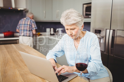 Senior woman using laptop and man working in kitchen