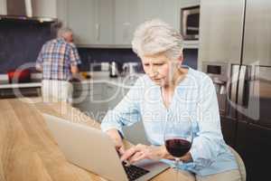 Senior woman using laptop and man working in kitchen