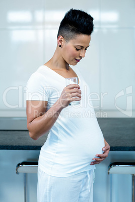 Pregnant woman drinking water in kitchen
