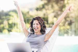 Excited young woman using laptop near poolside