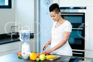 Portrait of pregnant woman cutting fruits on chopping board