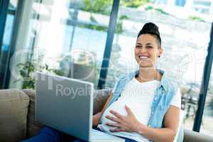 Portrait of pregnant woman relaxing on sofa with her laptop