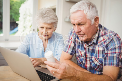 Senior couple holding a pill bottle while operating laptop