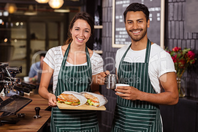 Smiling baristas holding sandwiches and hot milk