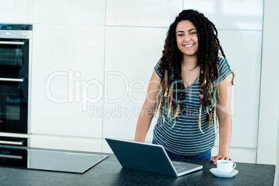 Portrait of woman leaning on worktop with laptop and tea cup in