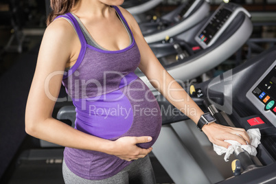 Mid section of pregnant woman cleaning treadmill