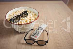 Bowl of popcorn, 3D glasses and television remote on table