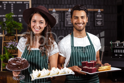 Smiling baristas holding trays with desserts