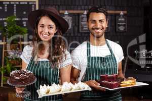 Smiling baristas holding trays with desserts