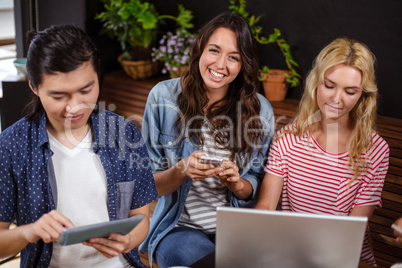 Smiling friends enjoying coffee together and using technologies