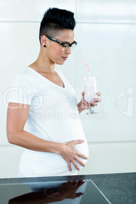 Pregnant woman drinking smoothie in kitchen