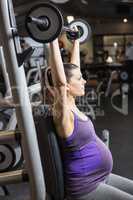 Determined pregnant woman lifting barbell