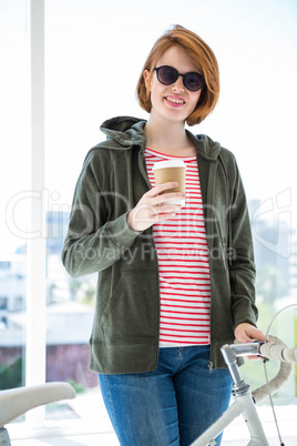 Cute hipster with her bike and disposable cup