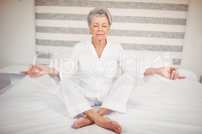 Senior woman meditating on bed