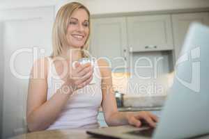 Pretty blonde woman having coffee and using laptop