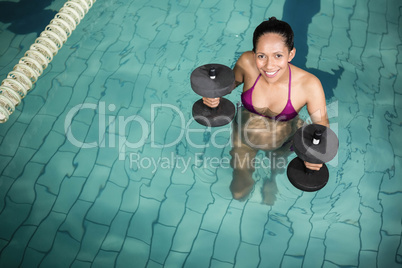Happy pregnant woman exercising in the pool with weights