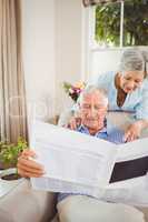 Senior woman talking to senior man reading newspaper