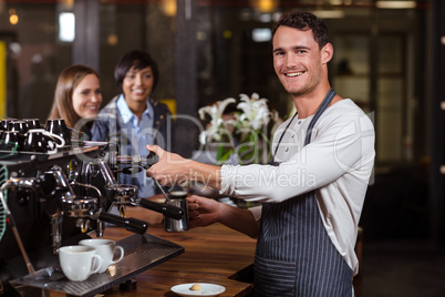 Smiling barista making hot milk with coffee machine