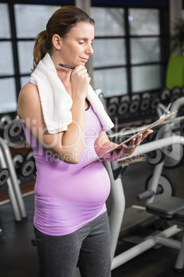 Pregnant woman in sportswear writing on a clibboard