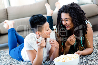 Lesbian couple lying on rug while having popcorn