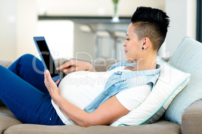 Pregnant woman relaxing on sofa with her digital tablet Pregnant woman relaxing on sofa with her digital tablet