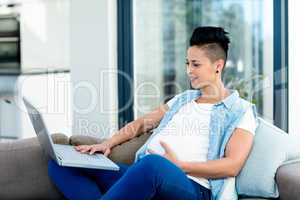 Pregnant woman relaxing on sofa with her laptop