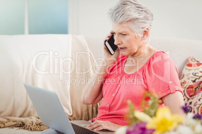 Senior woman talking on phone and using laptop