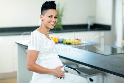 Portrait of pregnant woman sitting near kitchen worktop