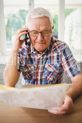 Senior man looking at a document while taking on phone