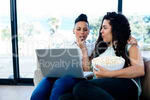 Woman feeding popcorn to her partner while using laptop