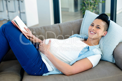 Portrait of pregnant woman reading a book while lying on sofa