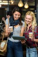 Smiling friends enjoying coffee while using tablet