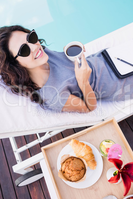 Young woman having cup of tea near poolside