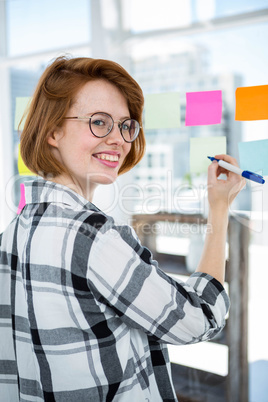 smiling hipster woman sticking notes on a notice board