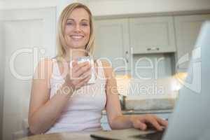 Pretty blonde woman having coffee and using laptop