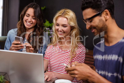 Smiling friends enjoying coffee together and using technologies