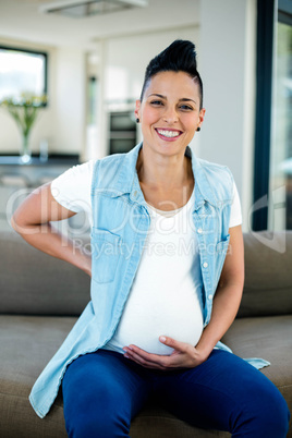 Portrait of pregnant woman sitting on sofa with and on stomach