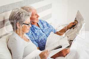 Senior woman reading magazine and senior man reading newspaper