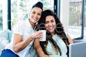 Portrait of happy lesbian couple having coffee and using laptop