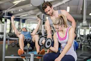 Trainer man helping woman lifting dumbbell