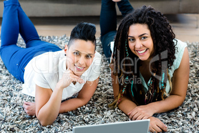 Portrait of lesbian couple lying on rug and using laptop