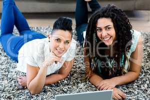 Portrait of lesbian couple lying on rug and using laptop